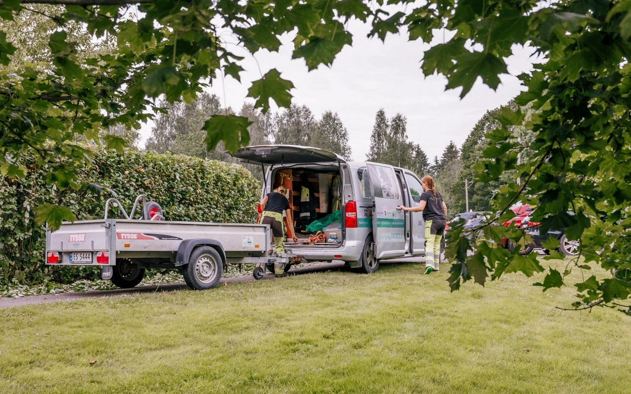 To anleggsgartnere på jobb henter utstyr fra varebil. De skal klippe hekk og gress.